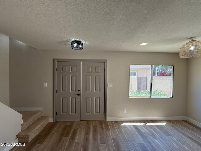 foyer entrance with wood finished floors, a textured ceiling, baseboards, stairs, and recessed lighting