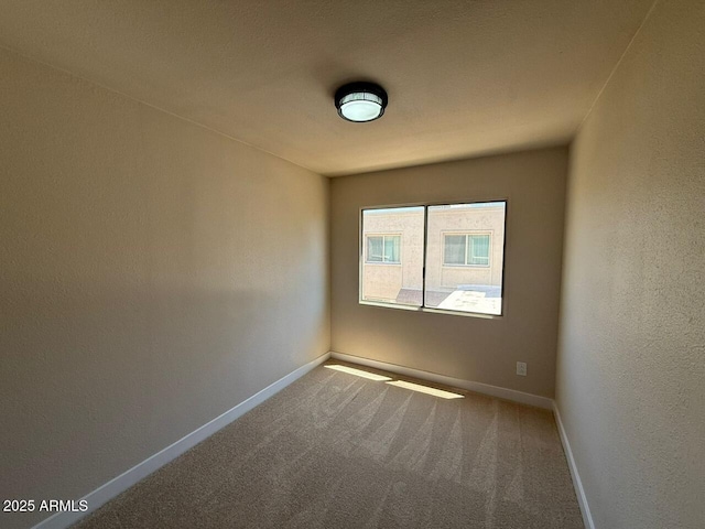 spare room with carpet, baseboards, and a textured wall