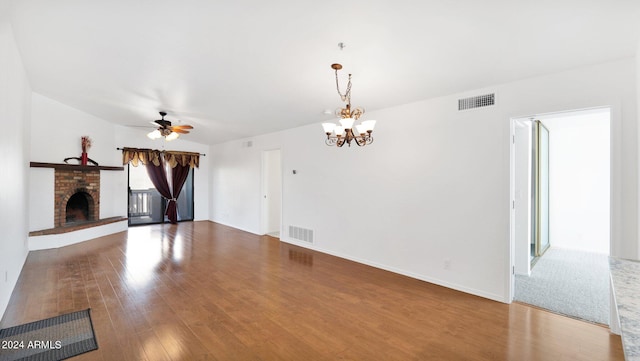 unfurnished living room with wood-type flooring, ceiling fan with notable chandelier, and a brick fireplace