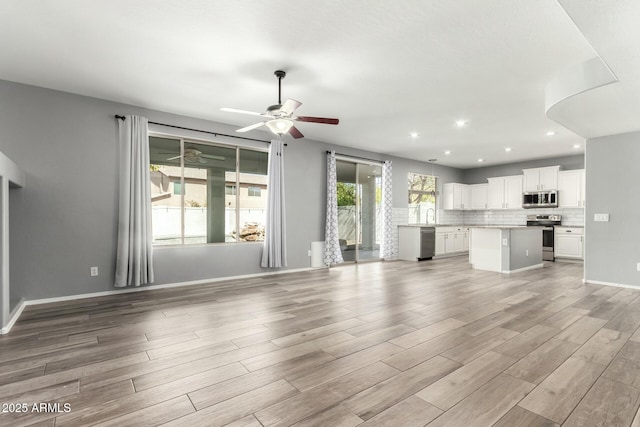 unfurnished living room featuring baseboards, light wood-style flooring, ceiling fan, a sink, and recessed lighting