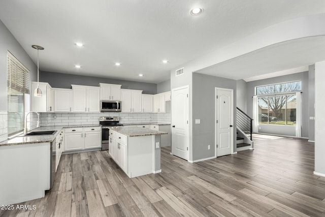 kitchen featuring light stone countertops, stainless steel appliances, a sink, backsplash, and a center island