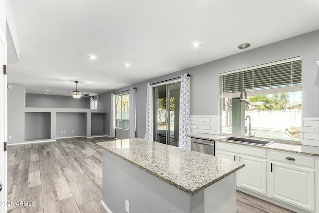 kitchen with a center island, light wood finished floors, stainless steel dishwasher, white cabinets, and a sink