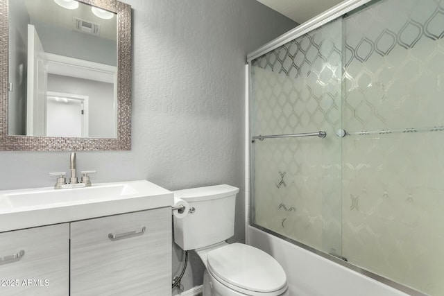 full bathroom featuring visible vents, a textured wall, toilet, combined bath / shower with glass door, and vanity