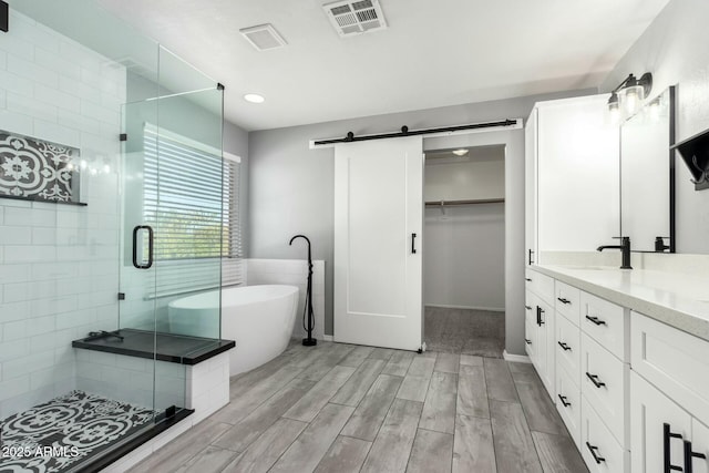 full bathroom with wood finish floors, visible vents, a freestanding bath, a shower stall, and vanity