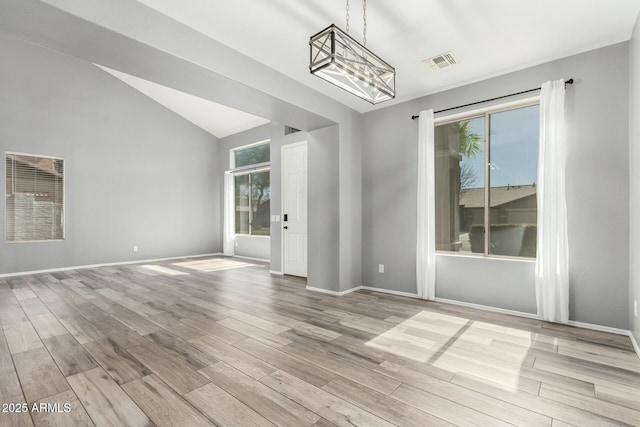 spare room with light wood-style floors, a healthy amount of sunlight, visible vents, and vaulted ceiling