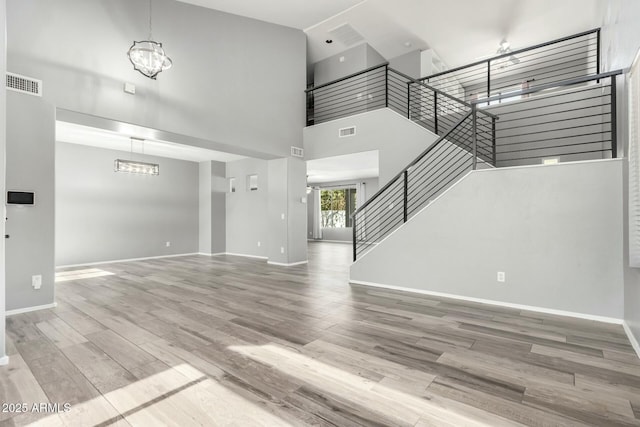 unfurnished living room featuring visible vents, stairway, a towering ceiling, and wood finished floors