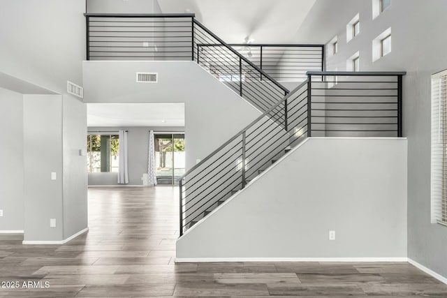 stairway featuring baseboards, a high ceiling, visible vents, and wood finished floors