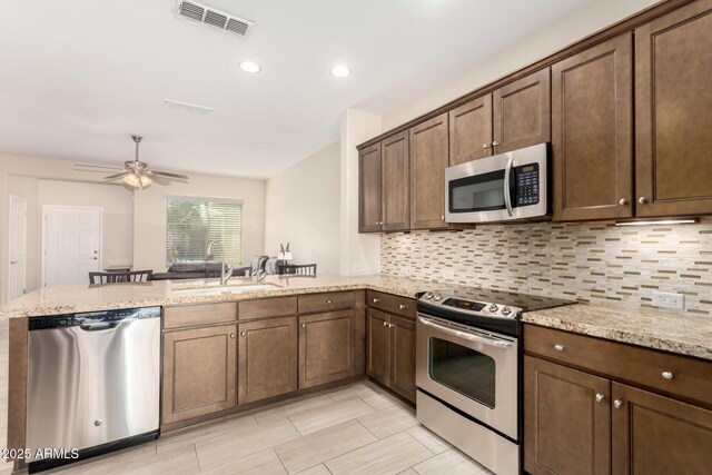 kitchen featuring light stone countertops, visible vents, a peninsula, stainless steel appliances, and decorative backsplash