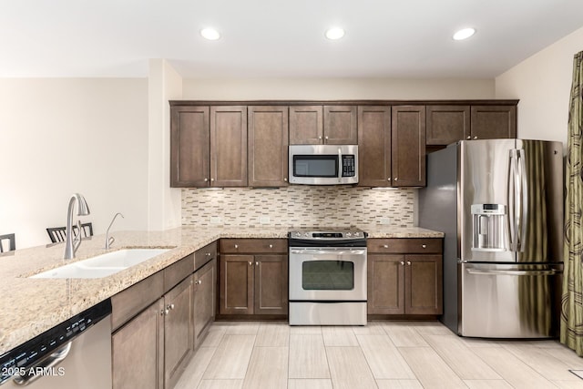 kitchen with dark brown cabinetry, appliances with stainless steel finishes, tasteful backsplash, and a sink