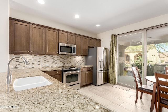 kitchen featuring backsplash, light stone counters, recessed lighting, appliances with stainless steel finishes, and a sink