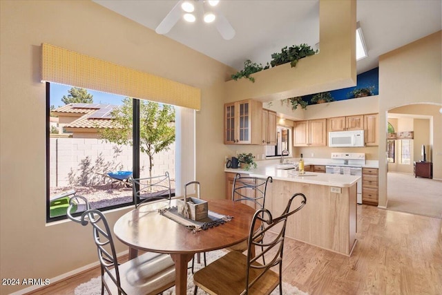 dining room featuring sink, a healthy amount of sunlight, a towering ceiling, and light hardwood / wood-style flooring