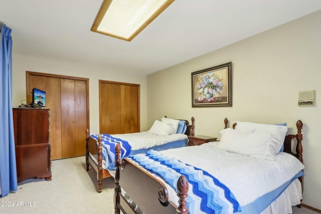 bedroom featuring light colored carpet and two closets