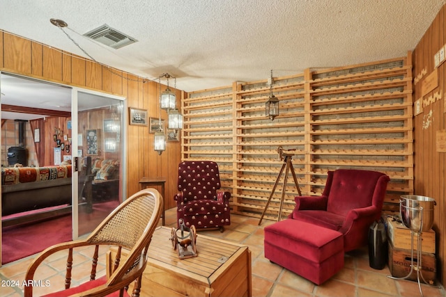 sitting room with a textured ceiling, a wood stove, wooden walls, and light tile patterned flooring