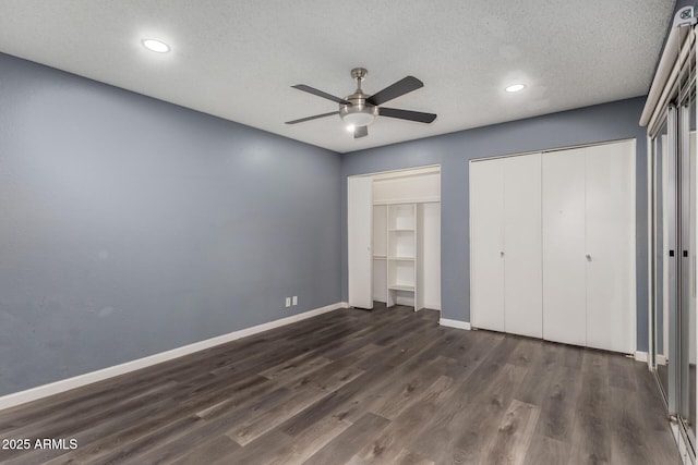 unfurnished bedroom featuring a textured ceiling, ceiling fan, multiple closets, and dark wood-type flooring