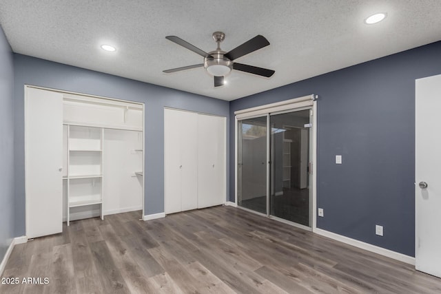 unfurnished bedroom with ceiling fan, two closets, a textured ceiling, and dark hardwood / wood-style floors