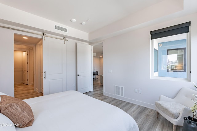 bedroom with a barn door and light hardwood / wood-style floors