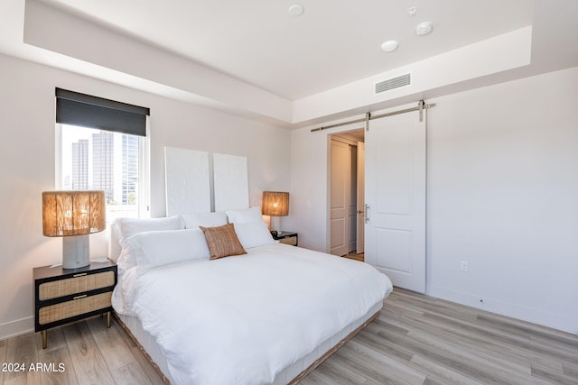 bedroom with a tray ceiling, a barn door, and light hardwood / wood-style floors