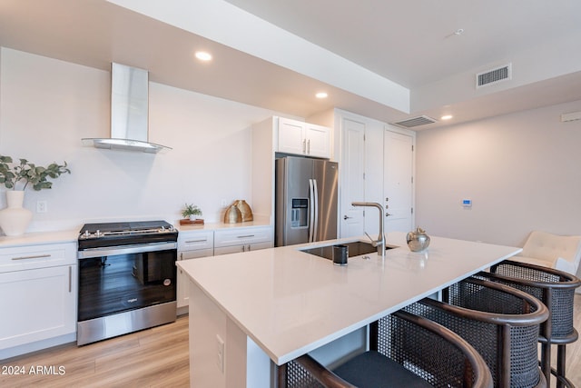 kitchen with appliances with stainless steel finishes, sink, wall chimney range hood, white cabinets, and an island with sink