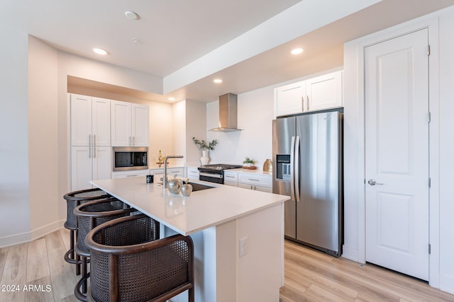 kitchen featuring stainless steel appliances, a kitchen island with sink, wall chimney range hood, light hardwood / wood-style flooring, and white cabinets