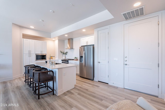 kitchen featuring a breakfast bar, stainless steel appliances, a kitchen island with sink, wall chimney range hood, and white cabinets