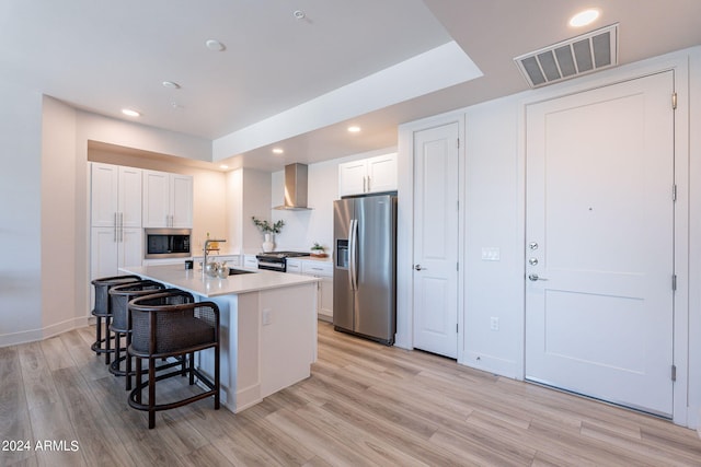 kitchen featuring white cabinetry, wall chimney range hood, a kitchen island with sink, and appliances with stainless steel finishes