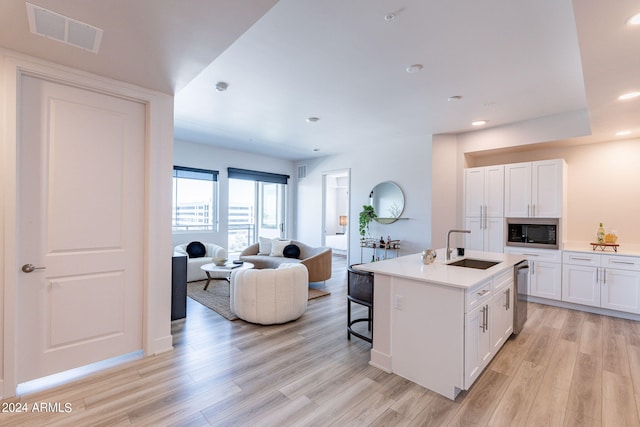 kitchen with white cabinetry, an island with sink, black microwave, and light hardwood / wood-style flooring