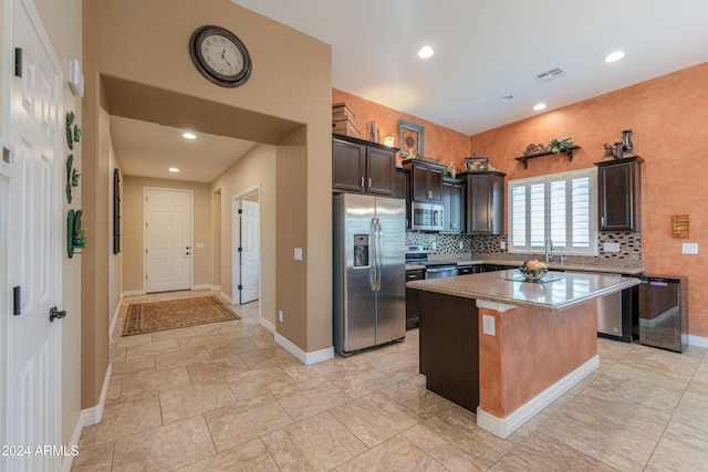 kitchen with dark brown cabinetry, sink, stainless steel appliances, tasteful backsplash, and a kitchen island