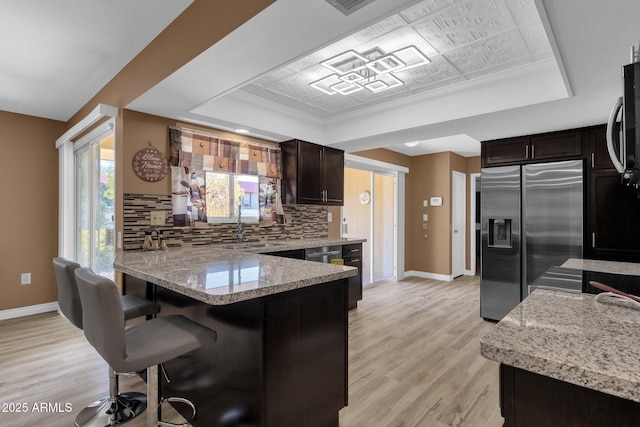 kitchen with appliances with stainless steel finishes, a tray ceiling, a kitchen breakfast bar, and backsplash