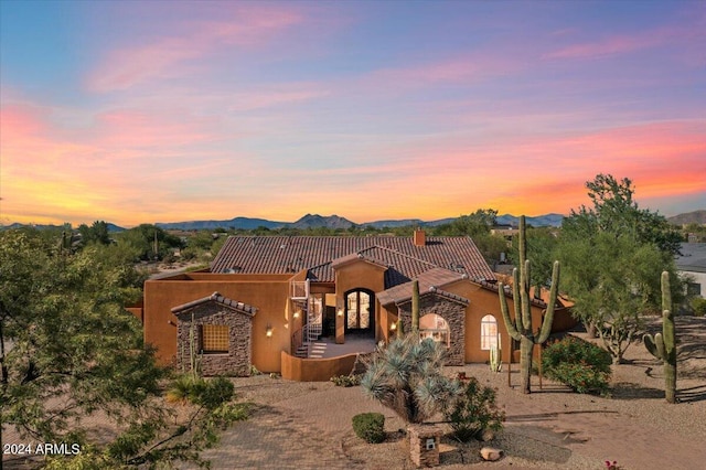 view of front facade with a tiled roof, a mountain view, decorative driveway, and stucco siding