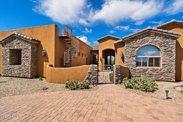 view of front of home featuring stone siding, a tile roof, a fenced front yard, a gate, and stucco siding