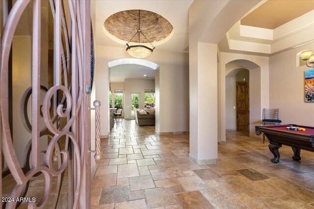 foyer with stone tile floors, arched walkways, baseboards, pool table, and a tray ceiling