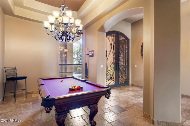 playroom featuring stone tile floors, arched walkways, a raised ceiling, and french doors