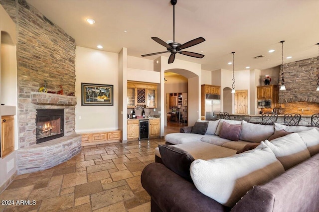 living area with arched walkways, stone tile flooring, a stone fireplace, a bar, and beverage cooler