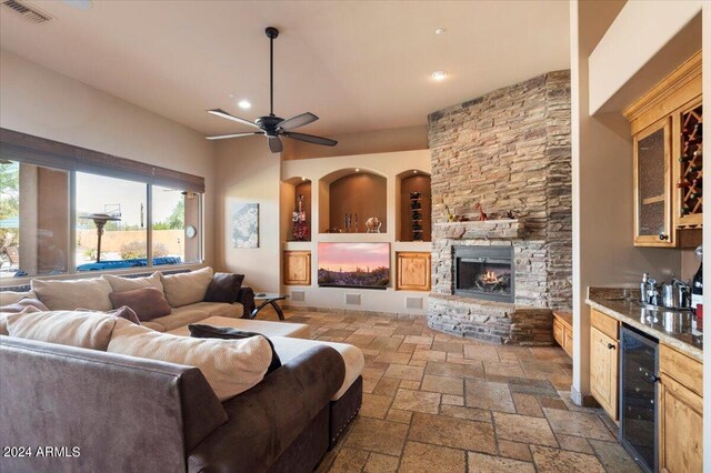 living area featuring beverage cooler, visible vents, stone tile flooring, a stone fireplace, and a bar