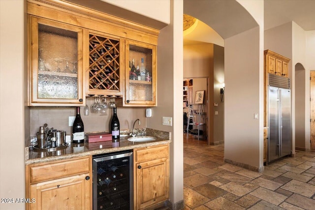 bar featuring wine cooler, stone tile floors, built in refrigerator, a sink, and wet bar