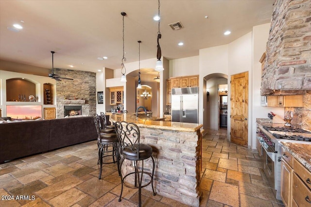 kitchen featuring visible vents, high end appliances, a kitchen breakfast bar, stone tile flooring, and a stone fireplace