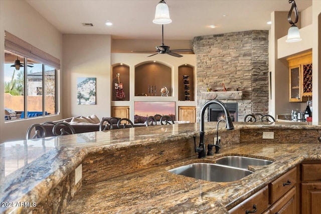 kitchen with visible vents, open floor plan, dark stone countertops, a stone fireplace, and a sink