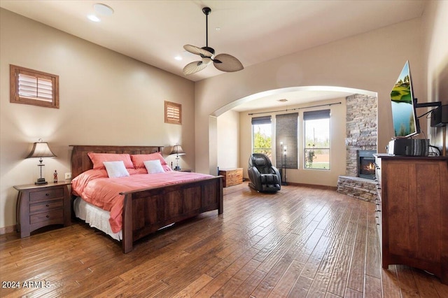 bedroom with arched walkways, a stone fireplace, hardwood / wood-style flooring, and recessed lighting