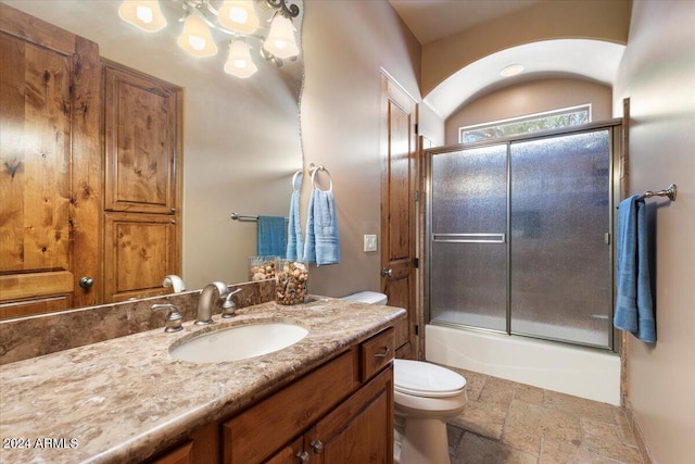 full bath featuring toilet, shower / bath combination with glass door, stone tile floors, and vanity