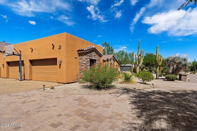 view of side of property featuring a garage, stone siding, driveway, and stucco siding