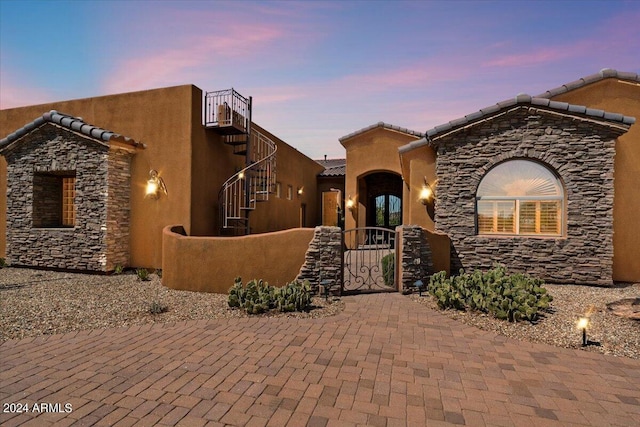 view of front of property featuring stone siding, a fenced front yard, a gate, and a tiled roof