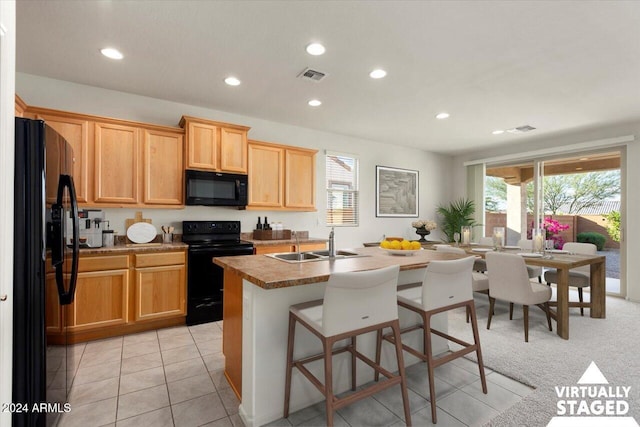 kitchen with black appliances, sink, a kitchen breakfast bar, light tile patterned floors, and a center island with sink