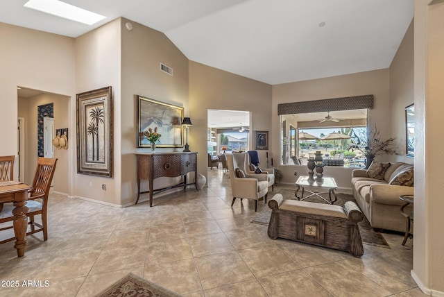 living room featuring high vaulted ceiling, a skylight, visible vents, and baseboards