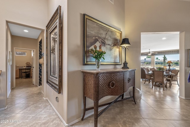 hall with light tile patterned floors, a high ceiling, baseboards, and recessed lighting