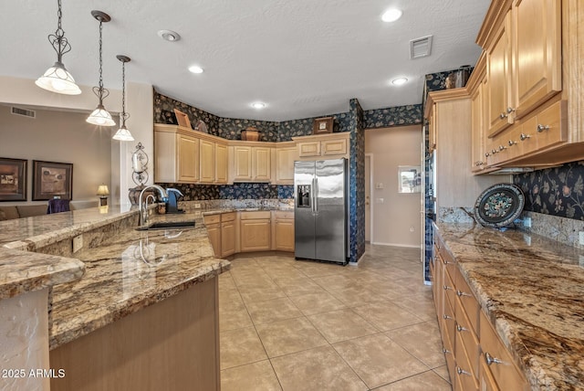 kitchen with visible vents, hanging light fixtures, light brown cabinetry, stainless steel refrigerator with ice dispenser, and a sink