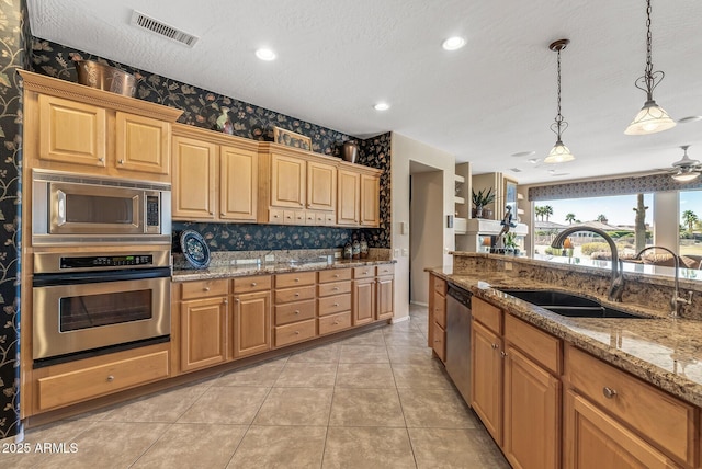 kitchen with decorative light fixtures, visible vents, appliances with stainless steel finishes, a sink, and light stone countertops