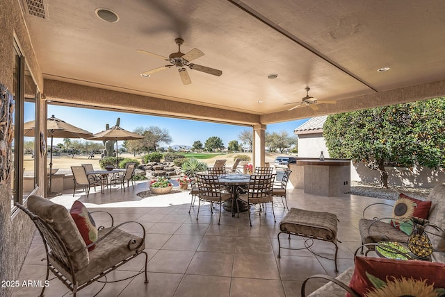 view of patio / terrace with a bar, outdoor dining space, exterior kitchen, and a ceiling fan