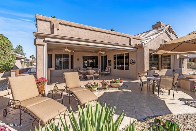 back of house with outdoor dining area, a ceiling fan, a tiled roof, stucco siding, and a patio area