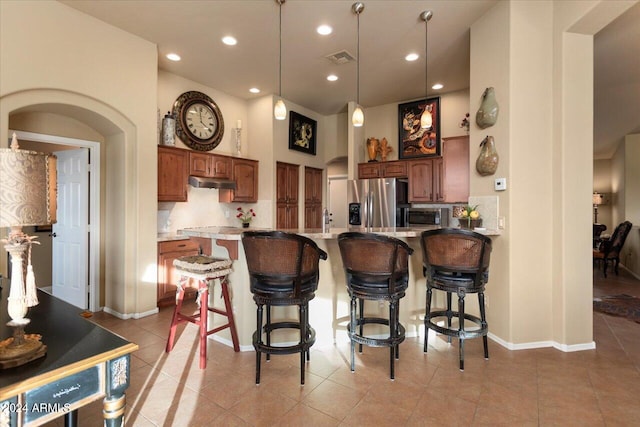 kitchen featuring tasteful backsplash, hanging light fixtures, appliances with stainless steel finishes, a breakfast bar, and light tile patterned flooring