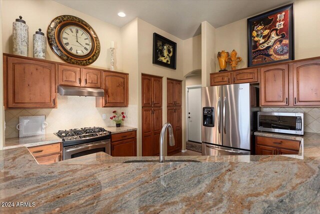 kitchen featuring backsplash, stainless steel appliances, light stone countertops, and sink